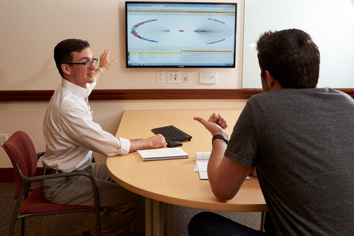 Two gentlemen view a screen with a graph on it.
