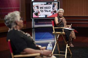 Claytee White sits in a chair and gestures toward a woman sitting to her right