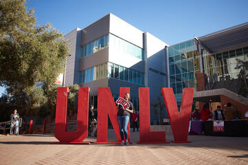 A student holds a UNLV sign in front of tall red UNLV letters
