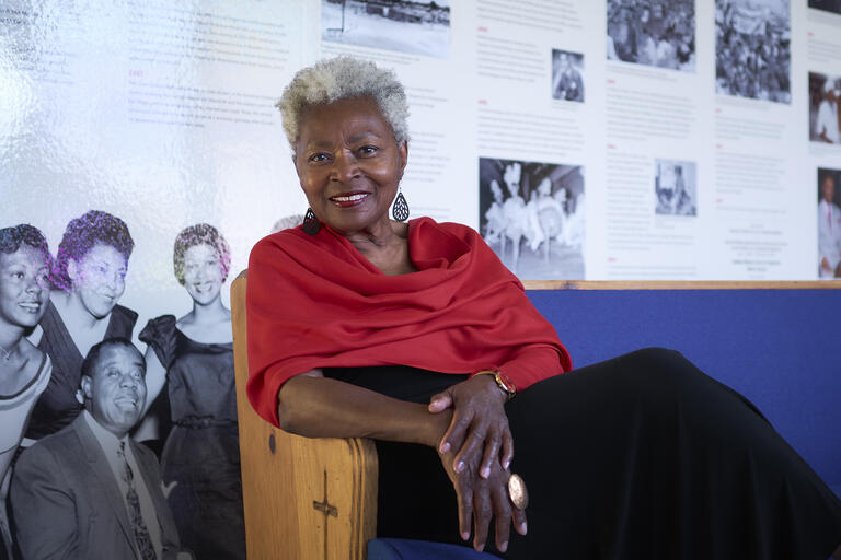 woman in red shawl sitting in front of wall of historic photos