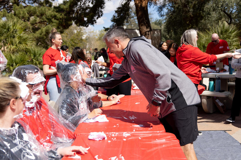 fundraising event where one woman sitting at a table is hit by a pie