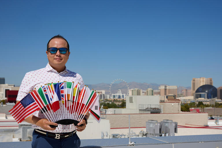 man with sunglasses holds multiple small country flags with Las Vegas Strip in the background