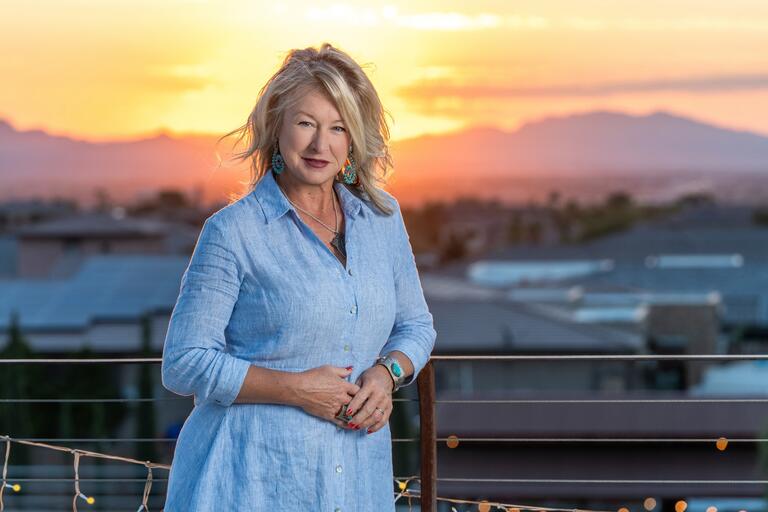 UNLV alumna Raquel Shohet Floyd poses in a light blue dress with the sun setting in the background