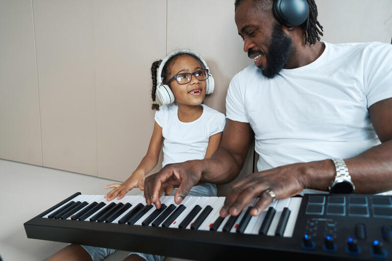 A father plays a synth piano with his daughter.