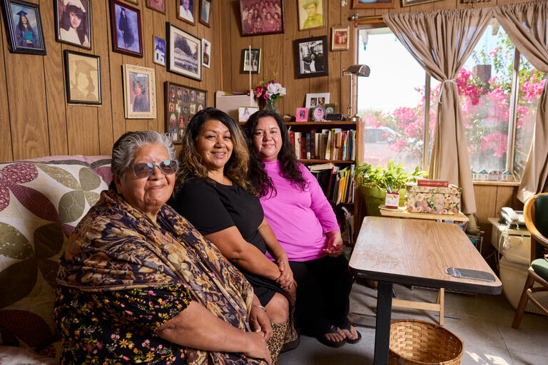 three women on couch in living room with walls covered in family photos