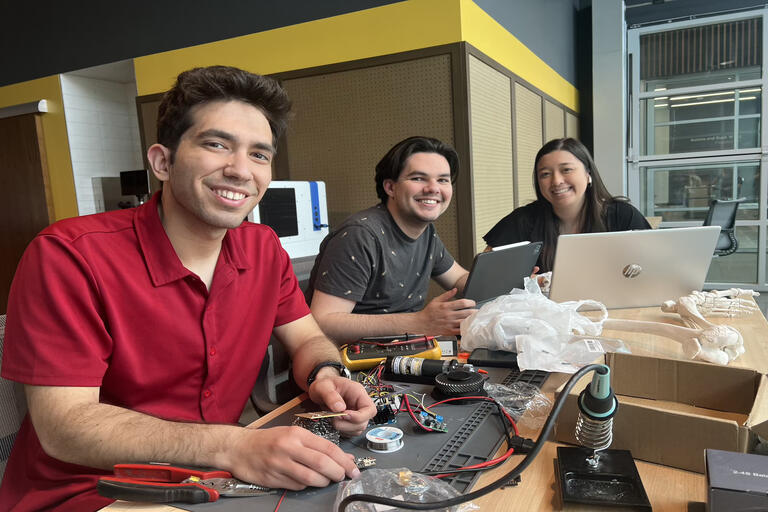 three students at table working on laptops