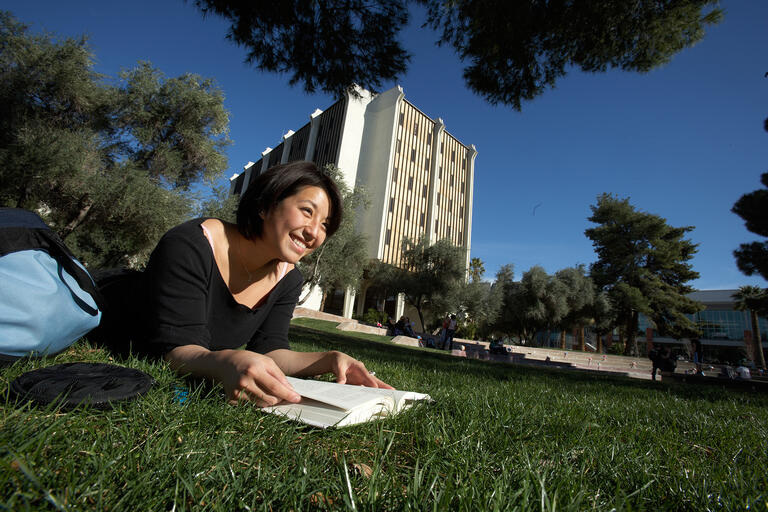 Student laid out on the grass and reading a book
